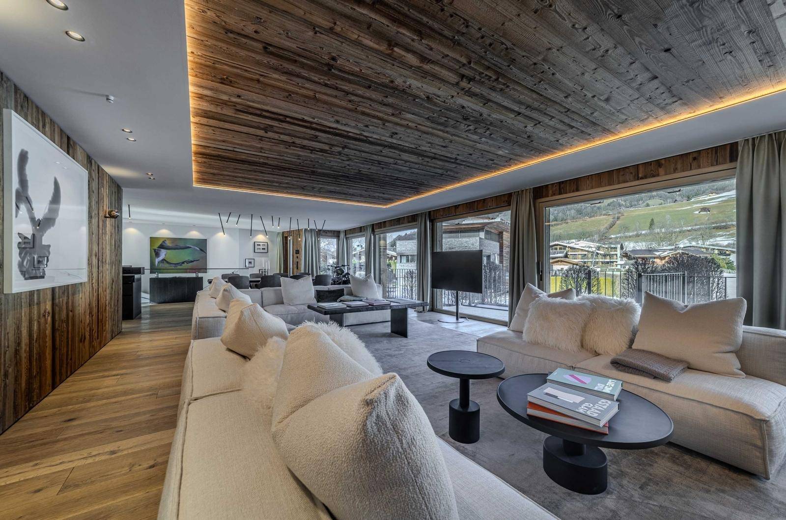 Luxuriöser Wohnbereich mit bequemen Sofas, Holzwänden und Decke sowie weitem Blick ins Grüne.