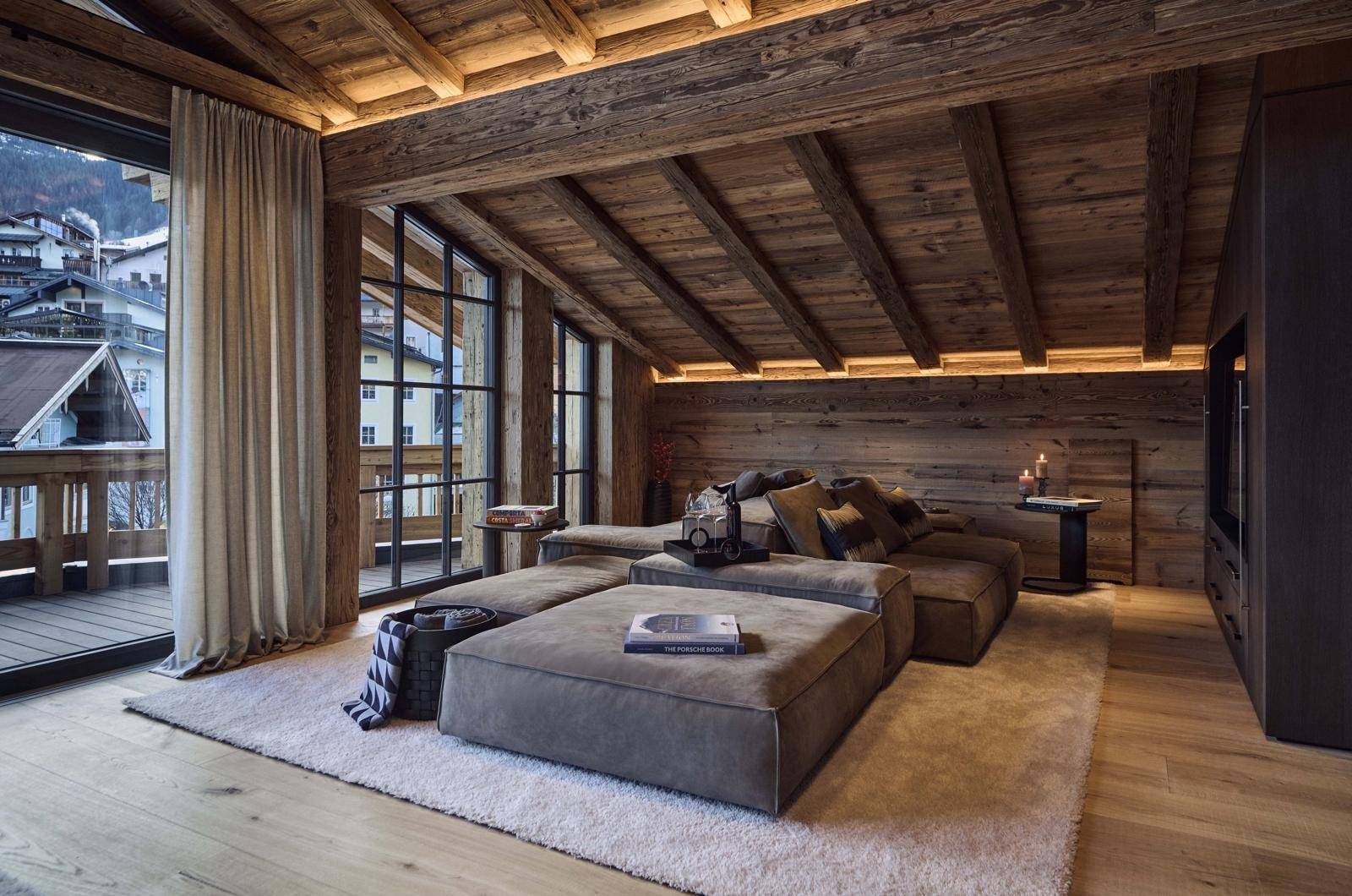 Schlafzimmer im Dachgeschoss mit Holzbalken, großen Fenstern und Zugang zu einem Balkon.