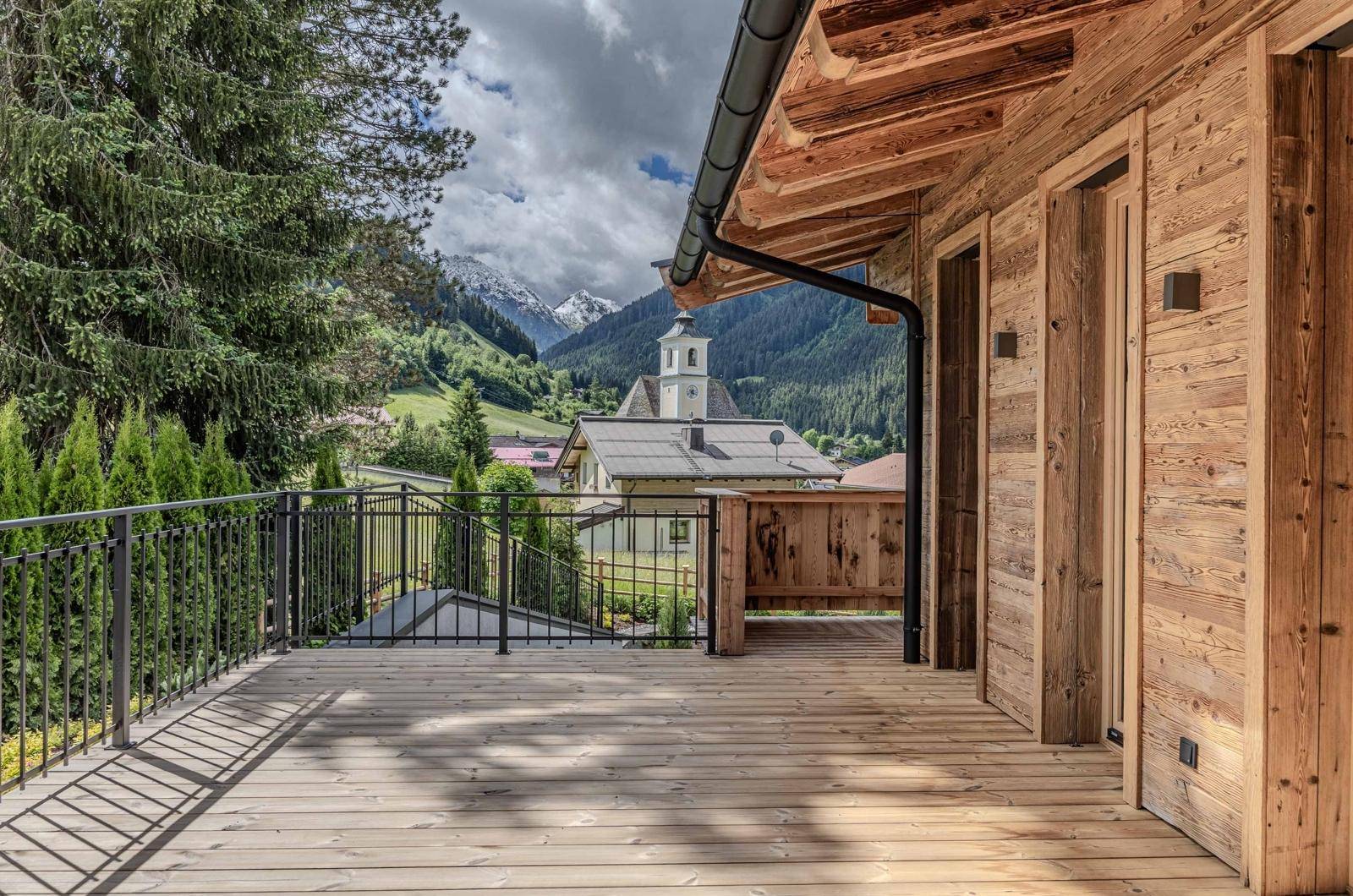 Geräumiger Holzbalkon mit Metallgeländer und malerischem Blick auf das Tal und die schneebedeckten Berge.