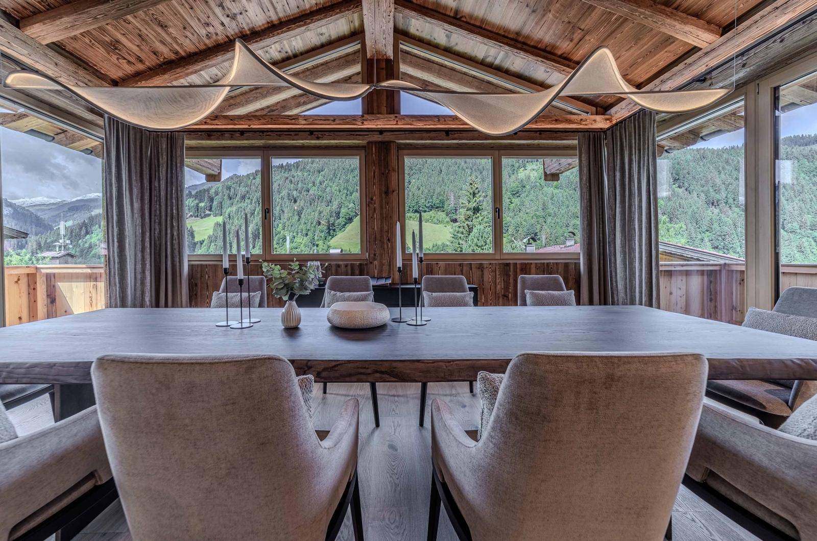 Eleganter Essbereich mit Holzbalkendecke, großem Esstisch und Panoramablick auf die bewaldeten Berge.