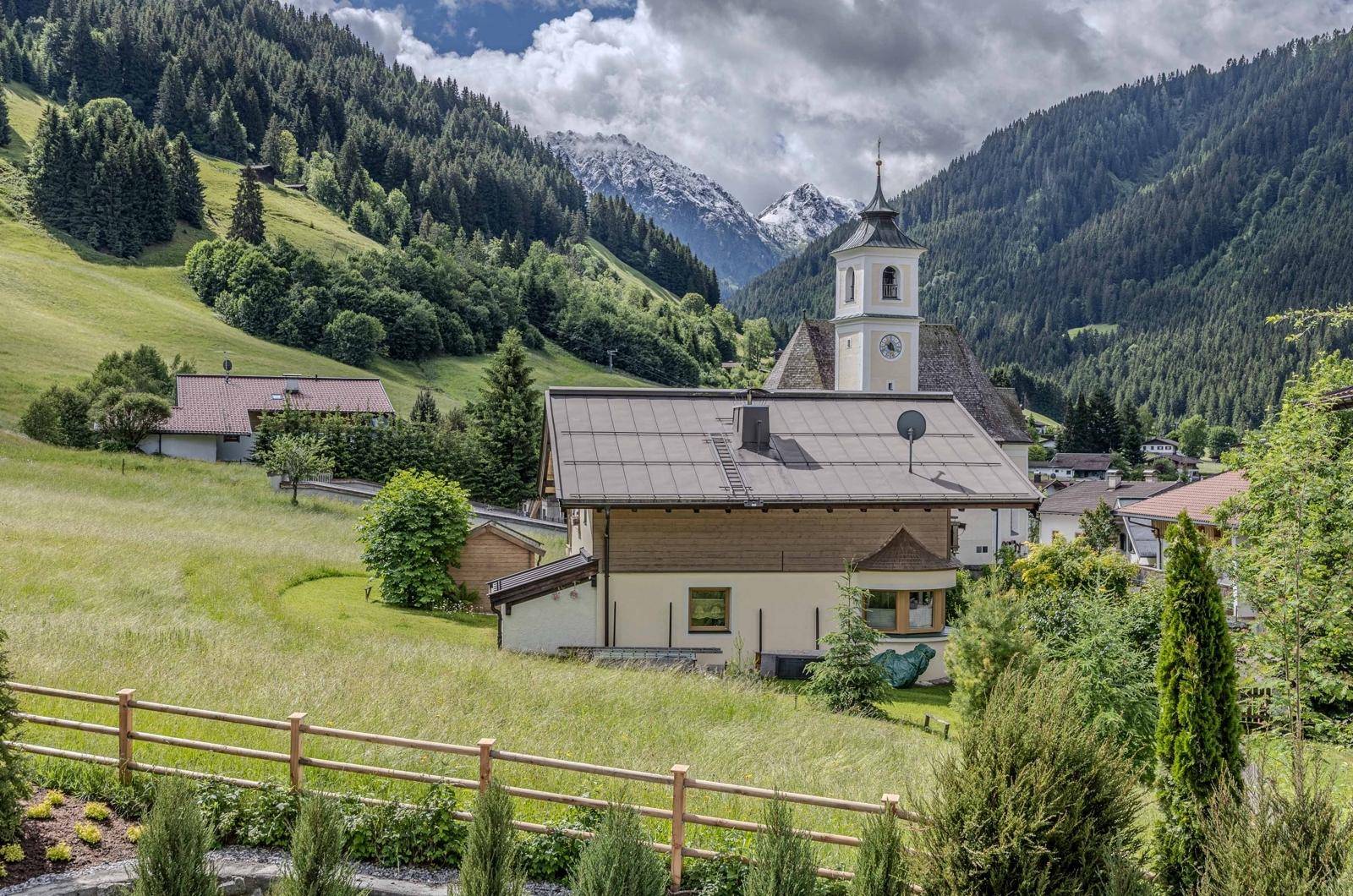 Malerische Aussicht auf ein Bergdorf mit Kirche und grünen Wiesen in den österreichischen Alpen.