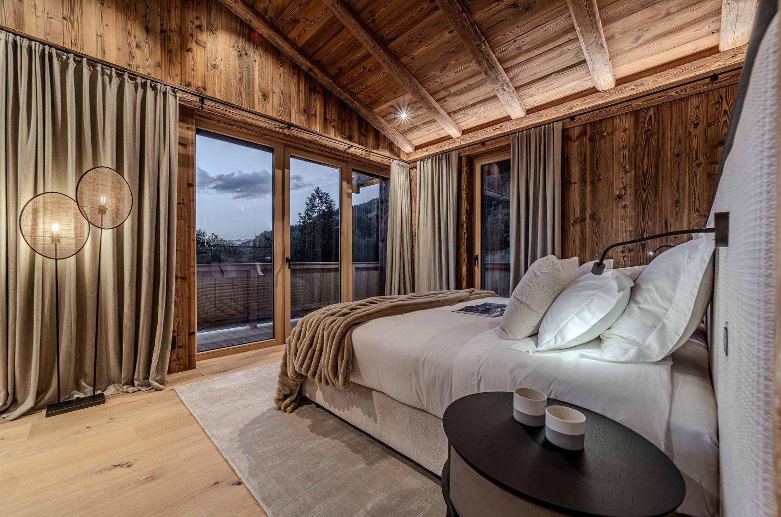 Schlafzimmer im alpinen Stil mit Holzwänden, Holzbalkendecke und direktem Zugang zum Balkon.