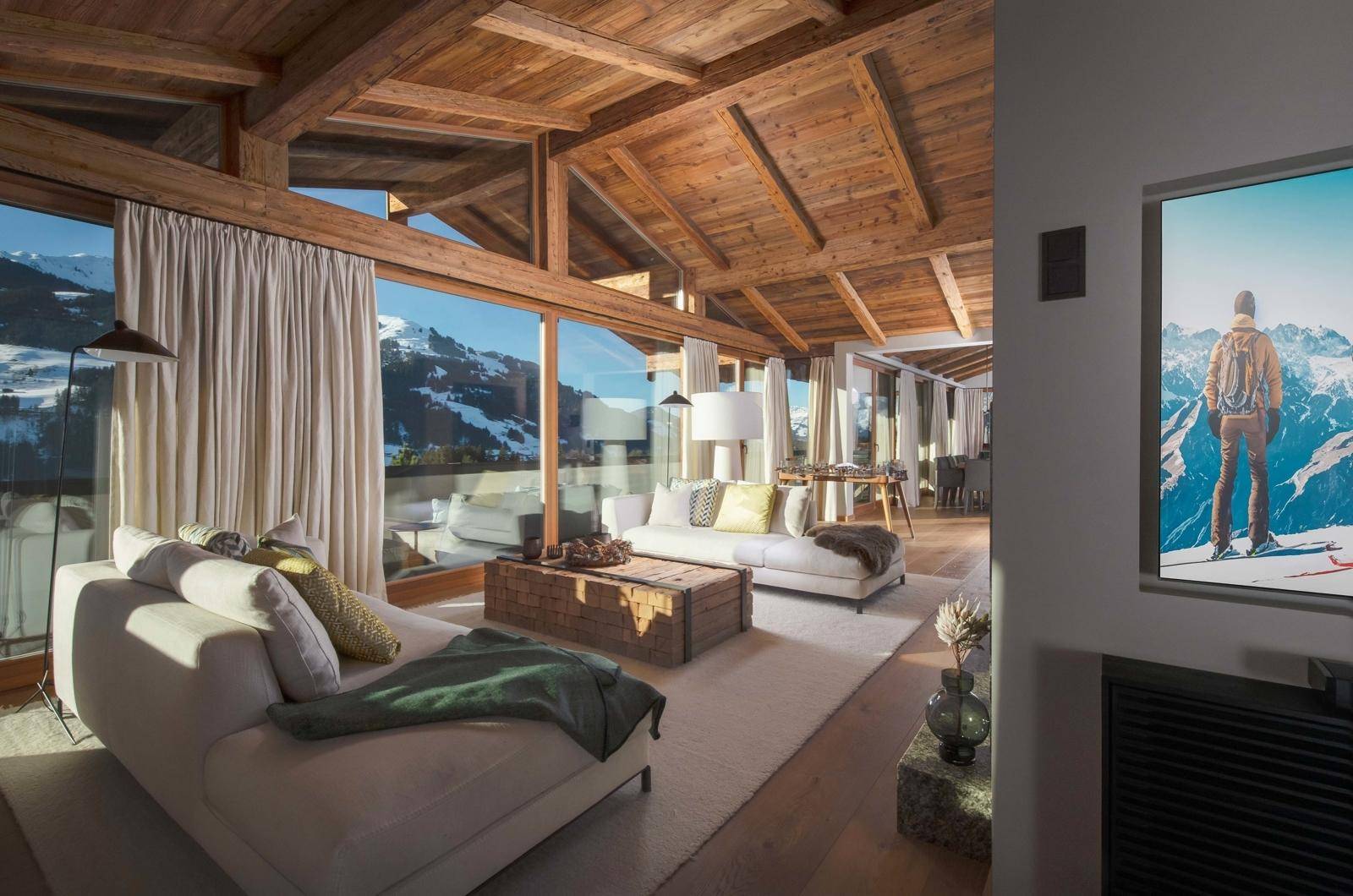 Lichtdurchflutetes Wohnzimmer mit hohen Holzdecken, großen Panoramafenstern und beeindruckendem Bergblick.