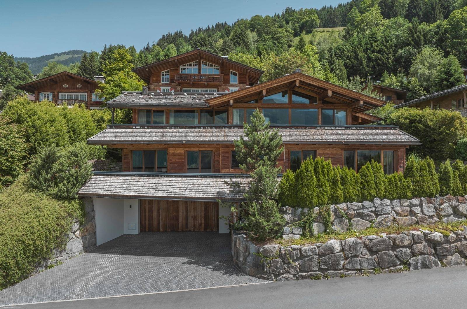 Elegantes Holzchalet mit großzügiger Auffahrt und integrierter Garage, umgeben von alpiner Landschaft.