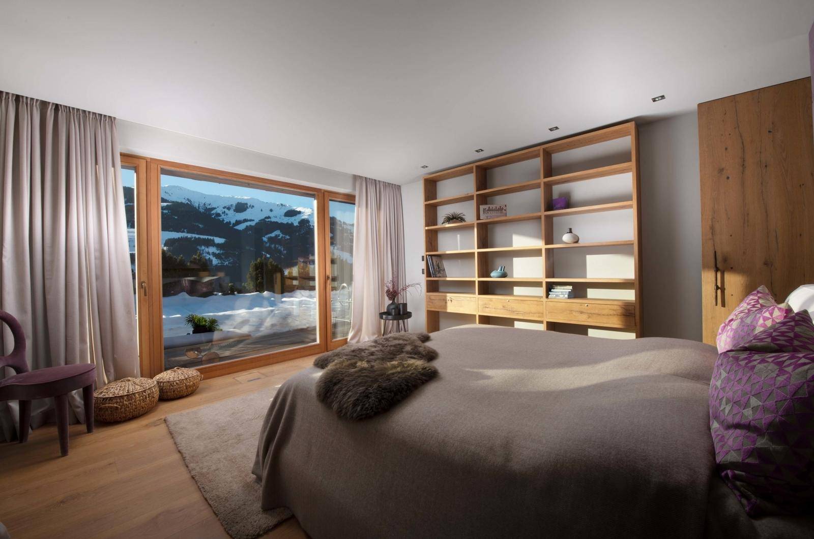 Helles Schlafzimmer mit großem Fenster, integriertem Bücherregal und direktem Zugang zur verschneiten Berglandschaft.