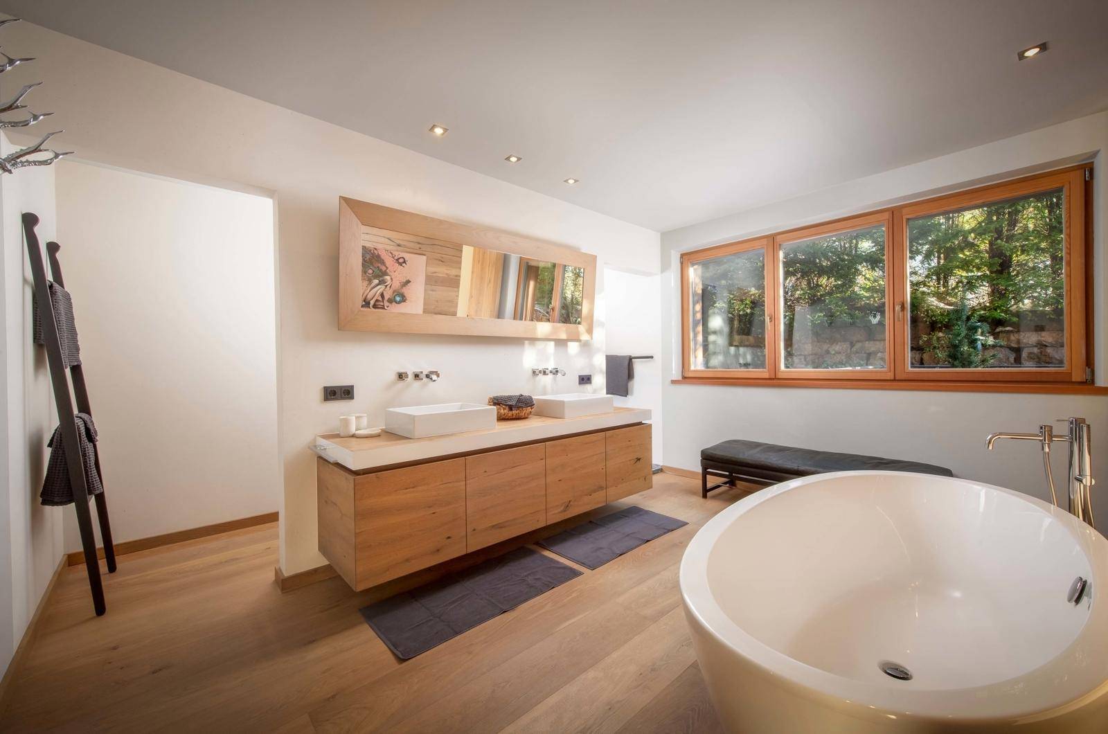 Modernes Badezimmer mit freistehender Badewanne, Doppelwaschbecken und Fenster mit Blick ins Grüne.