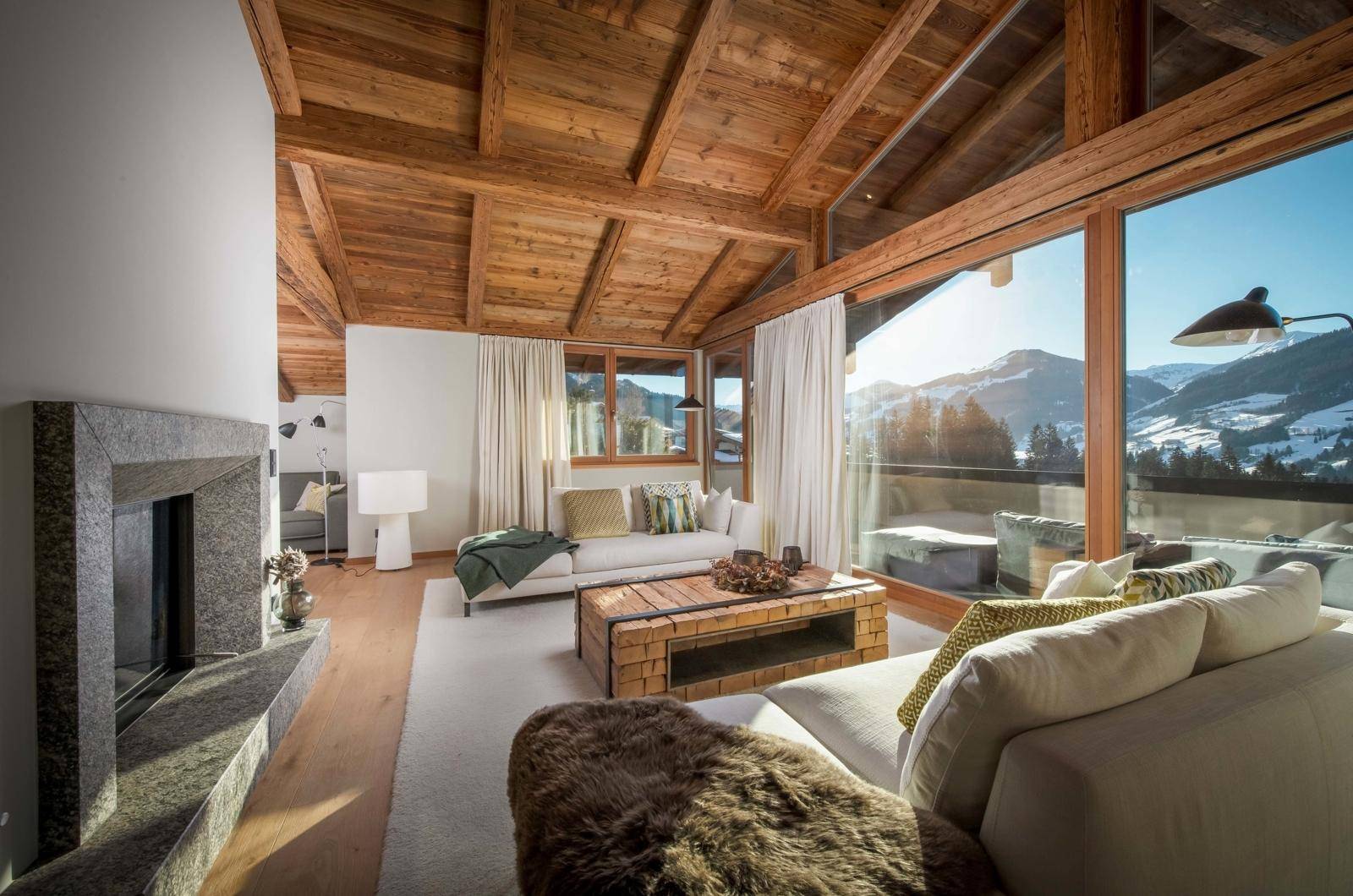 Gemütliches Wohnzimmer mit modernem Kamin, Holzbalkendecke und Panoramafenstern mit Bergblick.