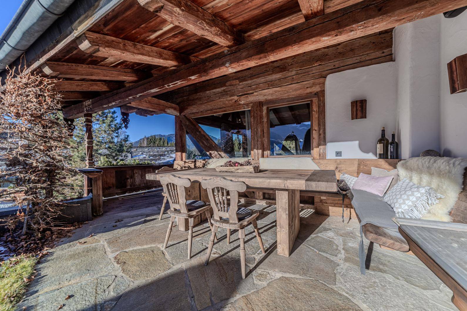 Überdachte Terrasse mit rustikalen Holzmöbeln, Steinboden und Blick auf die umliegende Berglandschaft.