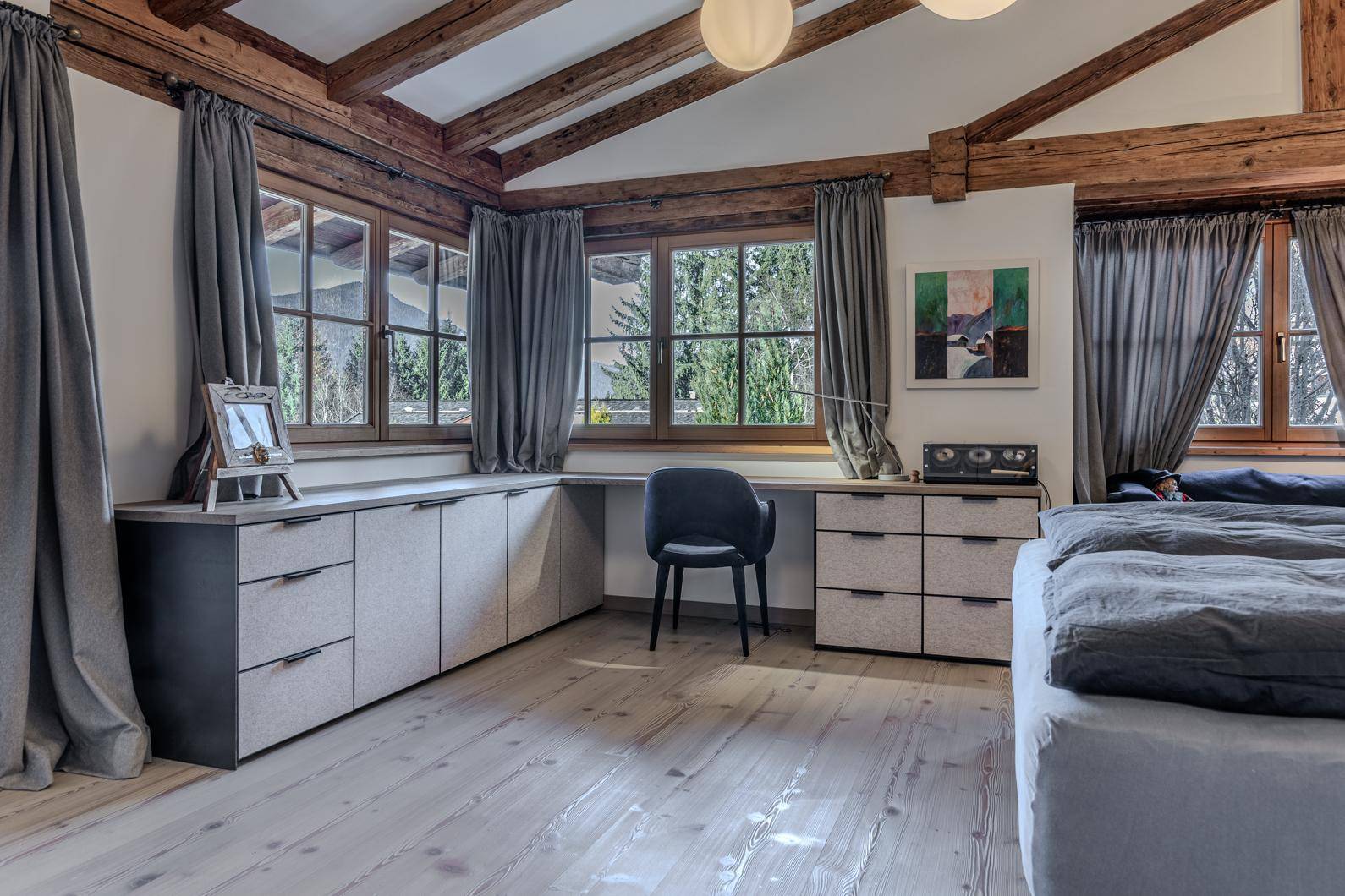 Schlafzimmer mit Holzboden, sichtbaren Balken, integriertem Schreibtisch und großen Fenstern.