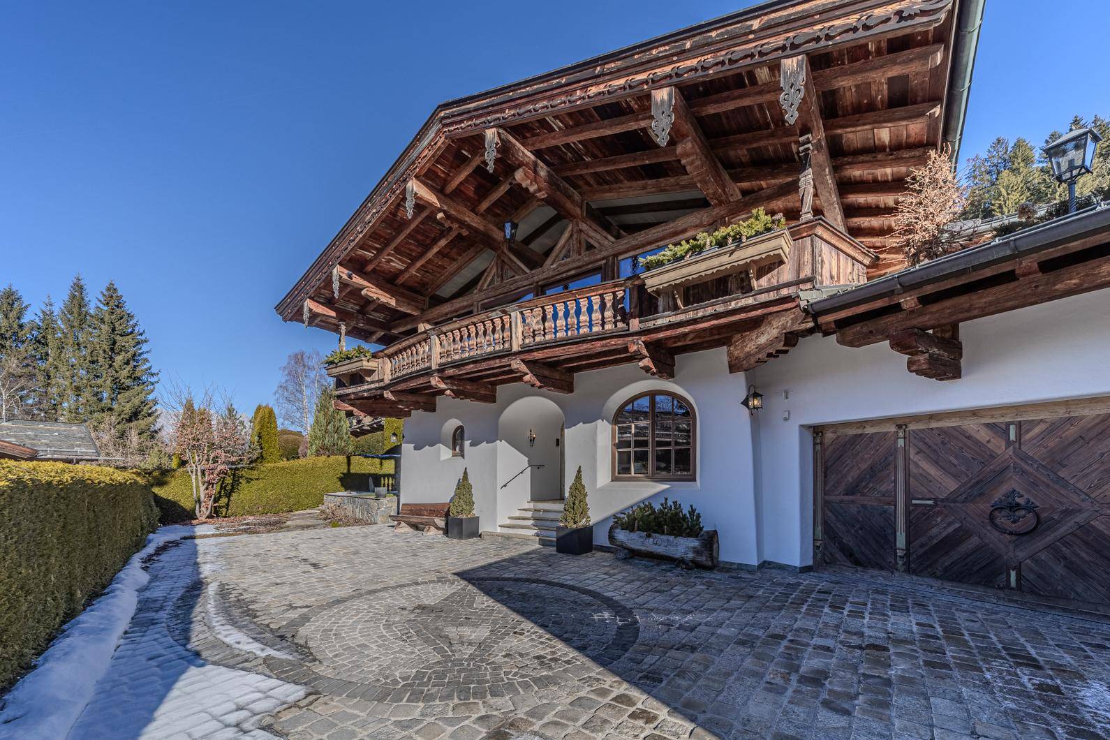 Beeindruckende Fassade eines Chalets im alpinen Stil mit Holzelementen und gepflasterter Auffahrt.
