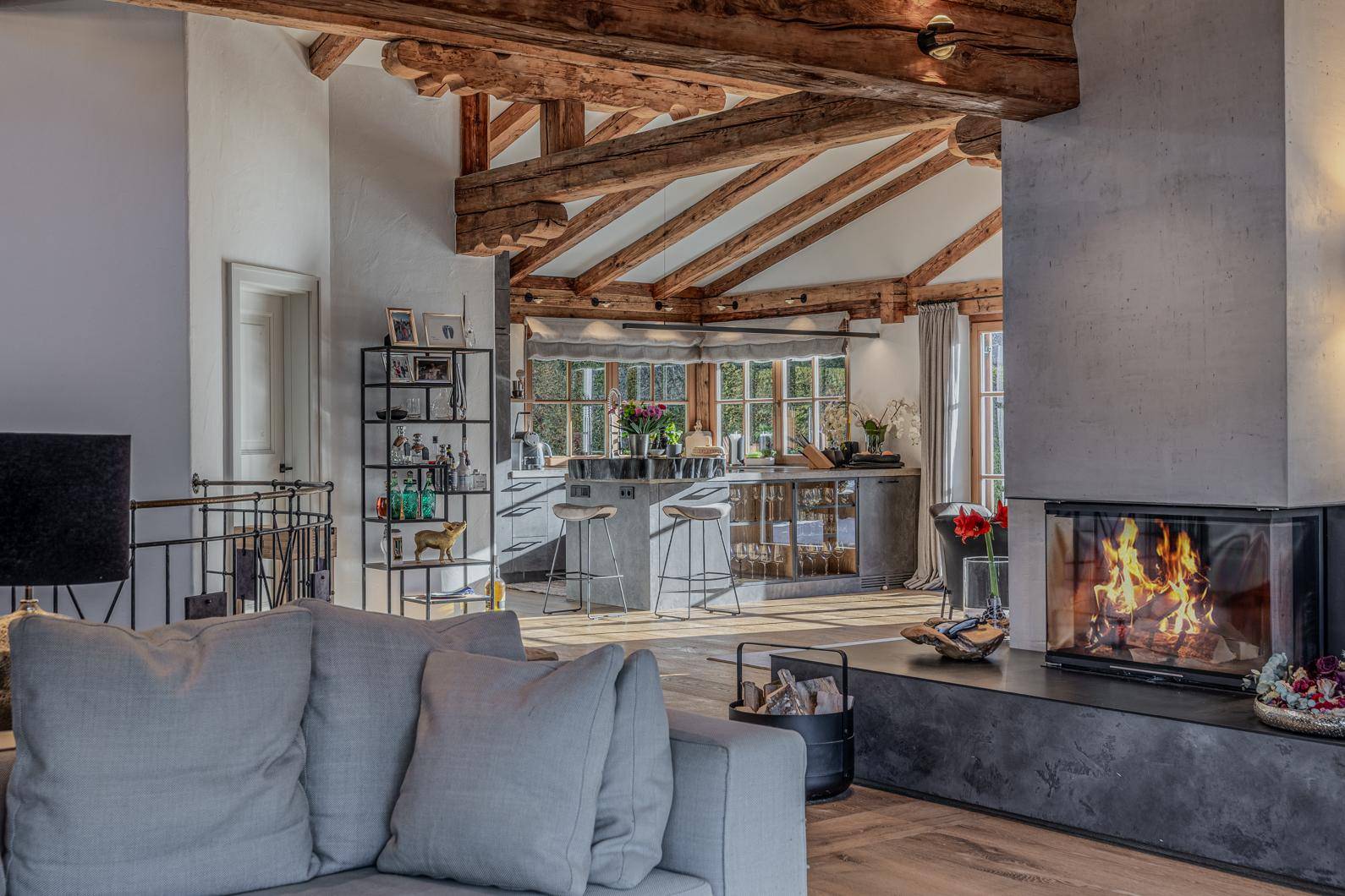 Gemütliches Wohnzimmer mit modernem Kamin, Holzbalken und offenem Übergang zur Küche.