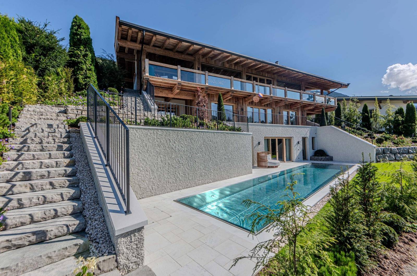 Moderne Holzarchitektur mit großzügigen Glasfronten, umgeben von alpiner Landschaft und einem Pool.