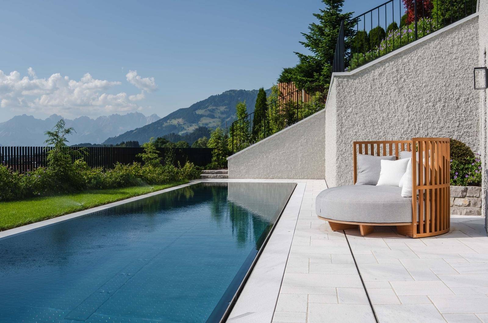 Sonniger Poolbereich mit stilvoller Liege und Panoramablick auf die grüne Berglandschaft.