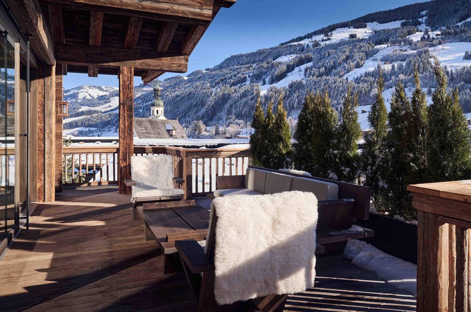 Sonnige Holzterrasse mit bequemen Sitzgelegenheiten und malerischem Blick auf die verschneite Berglandschaft.