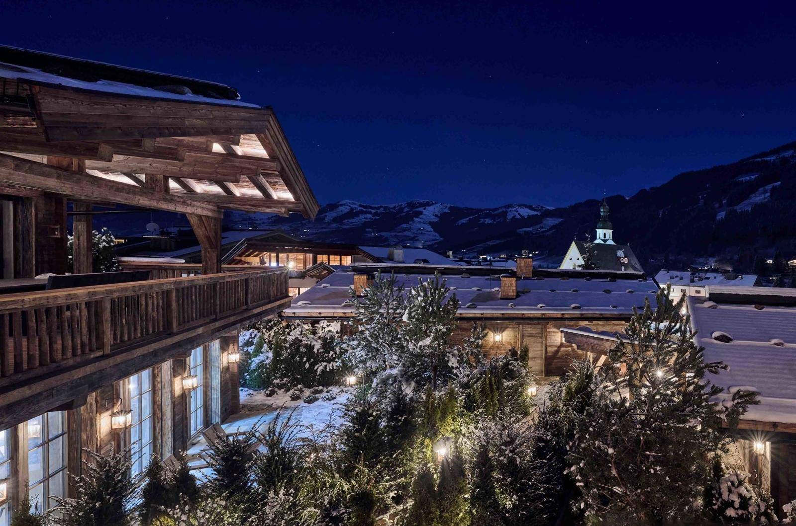 Beeindruckende Chalet-Fassade bei Nacht mit beleuchteten Balkonen und verschneiter Umgebung.