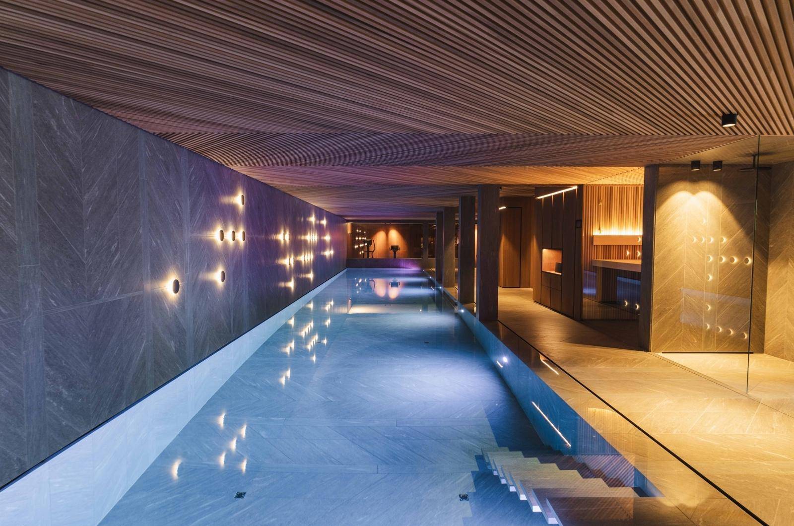 Exklusiver Innenpoolbereich mit stilvoller Beleuchtung, Steinwänden und einer eleganten Holzlamellendecke.