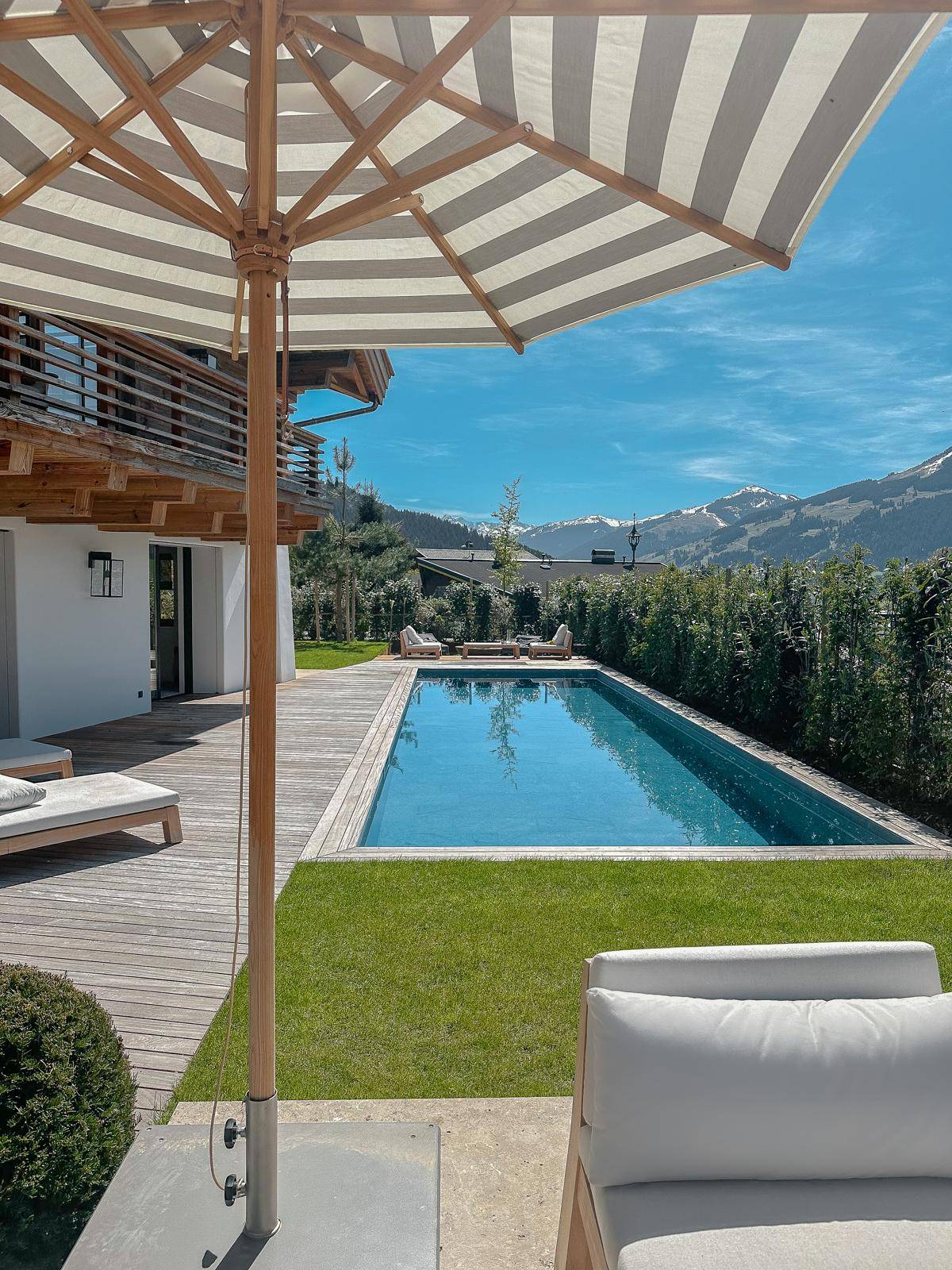 Gepflegter Gartenbereich mit Pool, Holzdeck und Liegestühlen unter blauem Himmel.