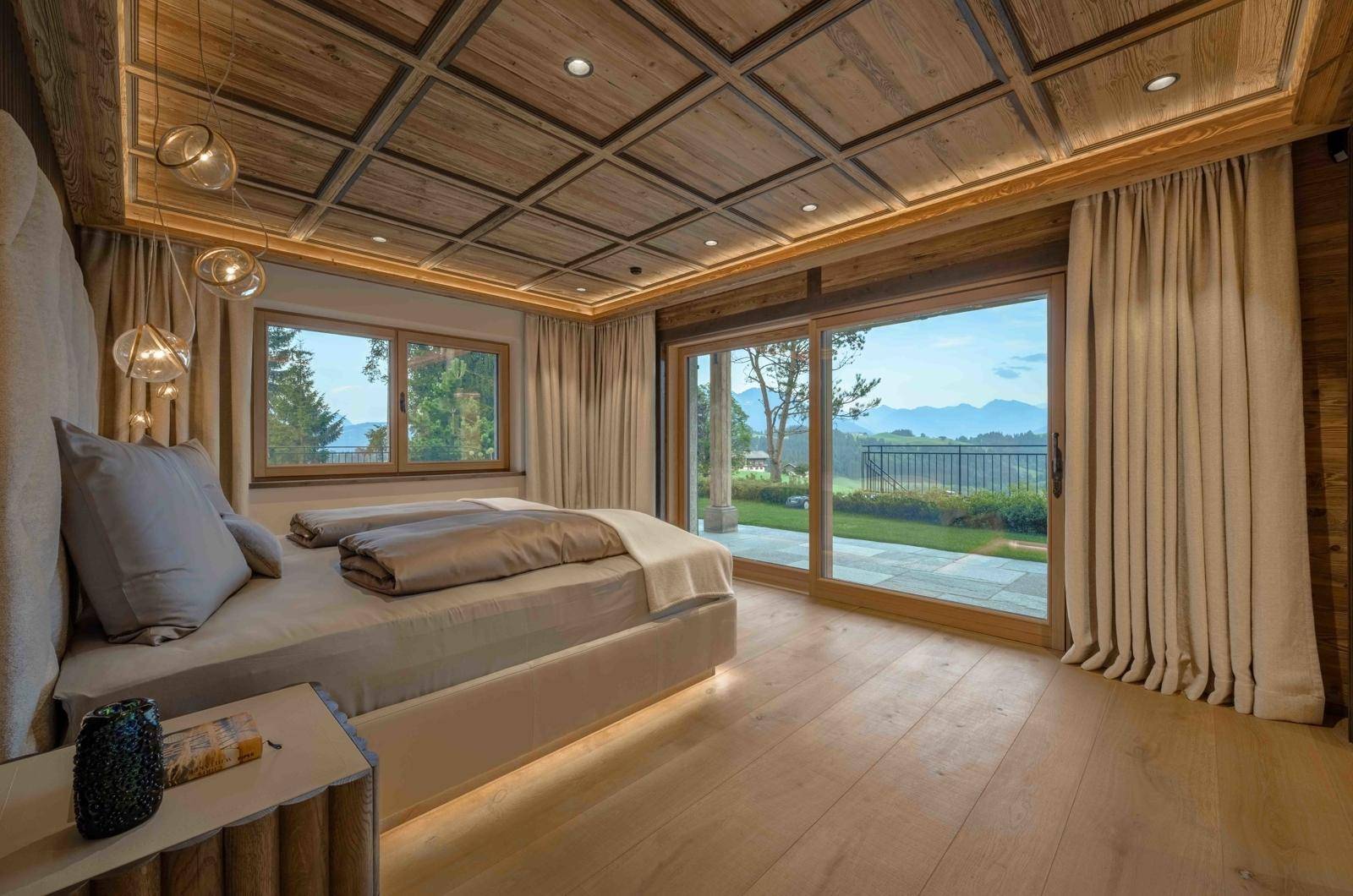 Helles Schlafzimmer mit Holzbalkendecke, großen Fenstern und Zugang zum Garten.
