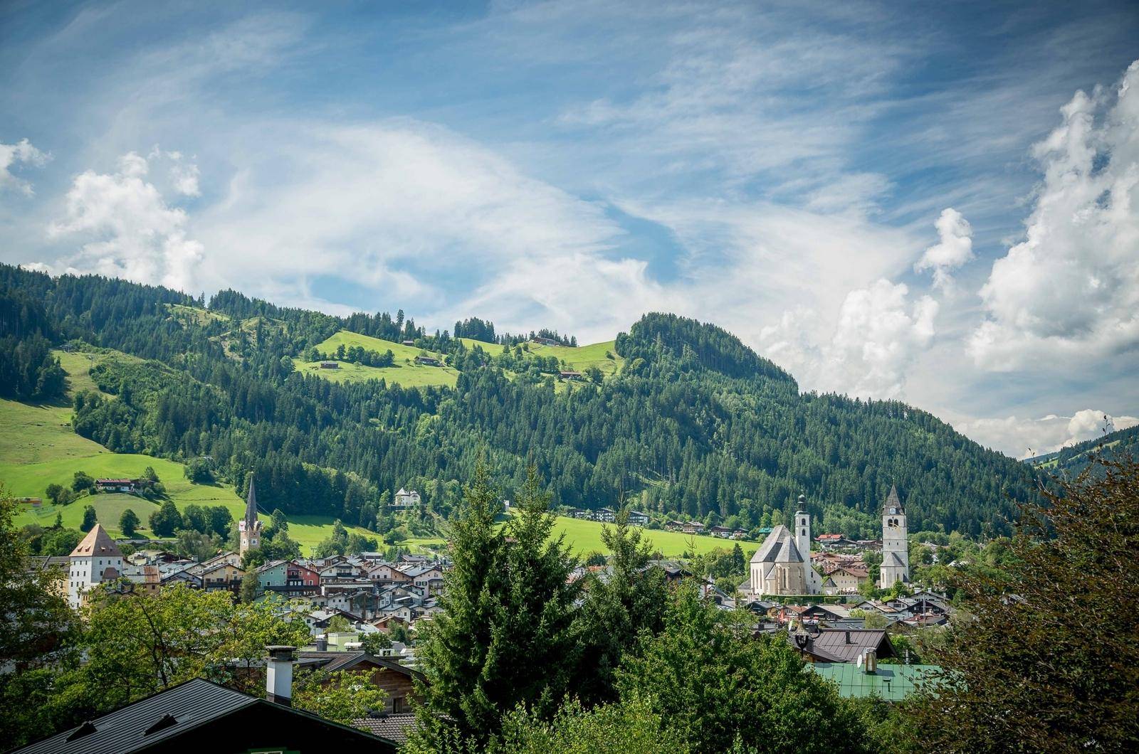 Malerischer Blick auf eine charmante Alpenstadt mit grünen Hügeln und bewaldeten Bergen im Hintergrund.