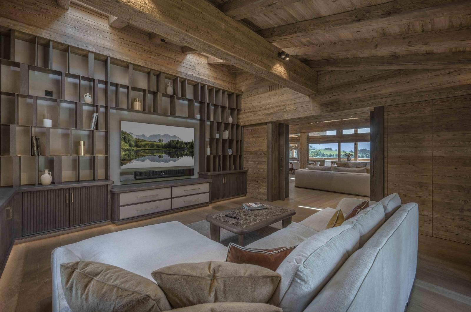 Gemütliches Wohnzimmer mit Holzbalkendecke, großem TV und integrierten Regalen.
