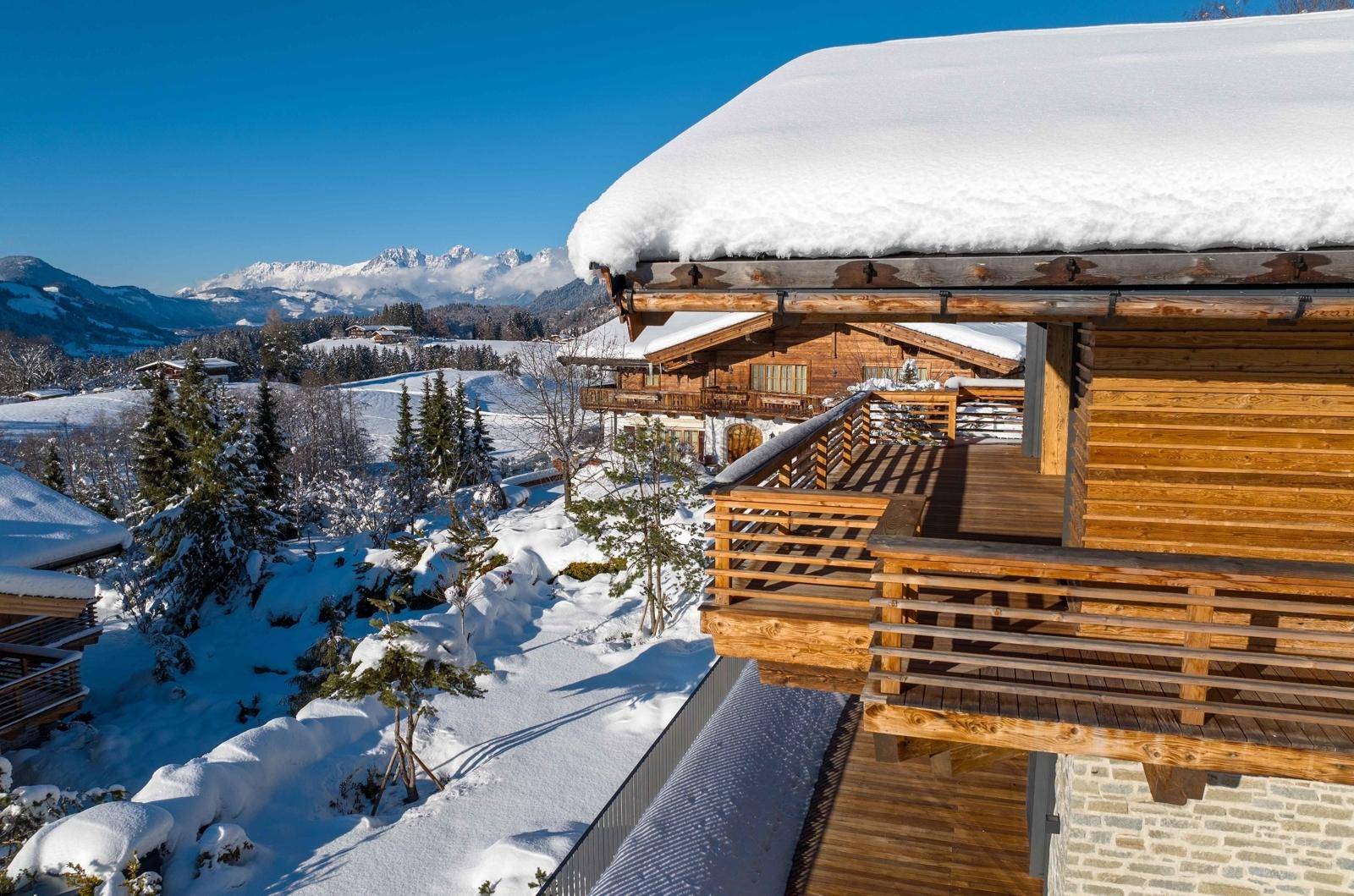 Holzbalcon mit weitem Blick über die verschneite Berglandschaft und andere Chalets.