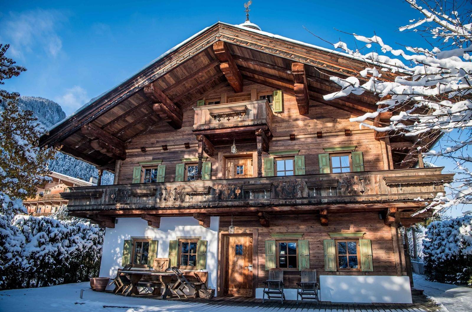 Traditionelles Holzchalet in verschneiter Berglandschaft mit mehreren Balkonen und grünen Fensterläden.
