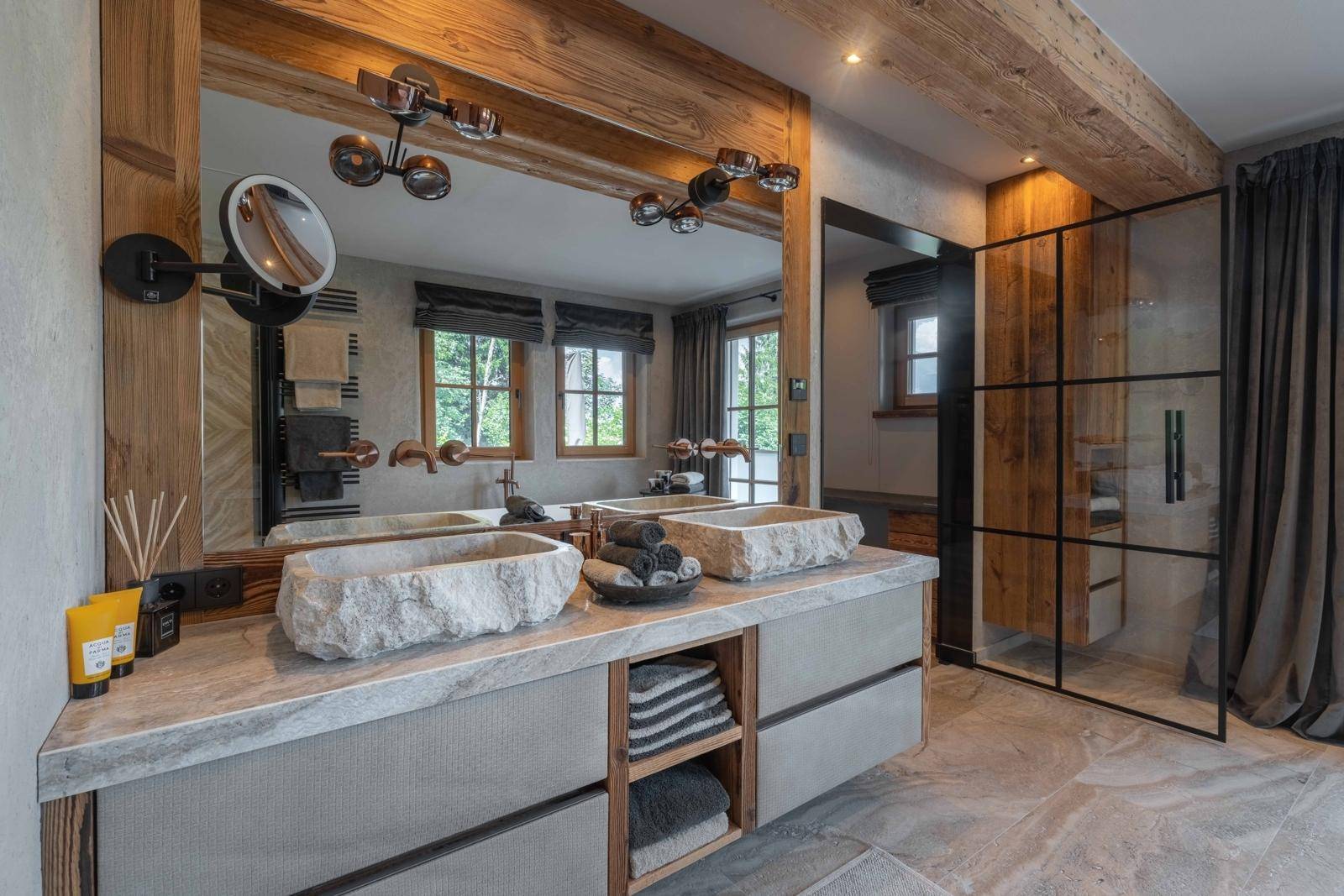 Luxuriöses Badezimmer mit Doppelwaschbecken aus Stein, begehbarer Dusche und Holzelementen.