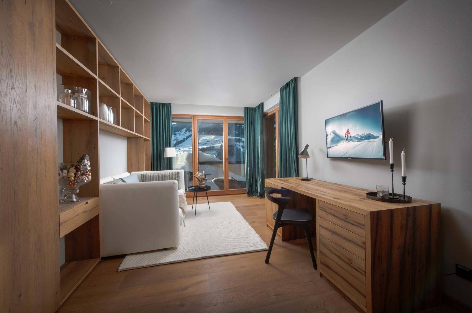 Helles Arbeitszimmer mit Sofa, Schreibtisch und großen Fenstern mit Blick auf die verschneite Bergwelt.