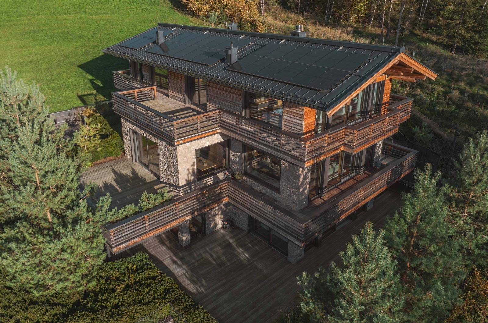 Architektonisch ansprechendes Chalet mit Holzfassade, mehreren Balkonen und integrierten Solarpaneelen auf dem Dach.