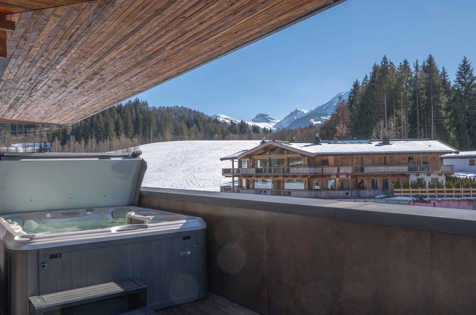 Balkon mit Whirlpool und Panoramablick auf die verschneiten Berge und die umliegende Natur.
