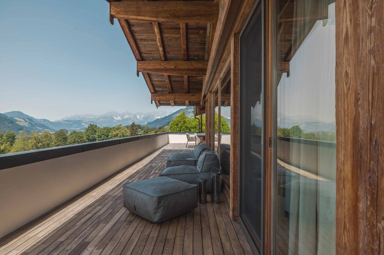 Geräumiger Holzbalkon mit bequemen Lounge-Möbeln und atemberaubendem Panoramablick auf die Berge.
