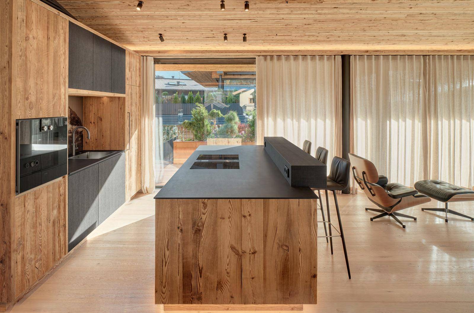 Moderne Holzküche mit Kochinsel, integrierten Geräten und Zugang zu einer Außenterrasse.