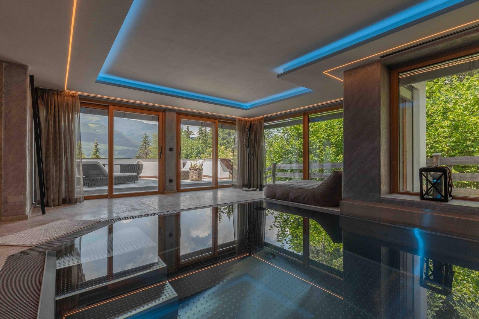 Moderner Innenpoolbereich mit großen Fenstern, Bergblick und stimmungsvoller Beleuchtung.