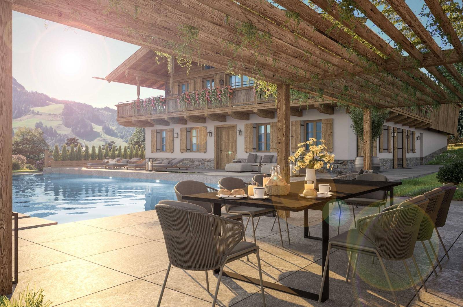 Sonnige Terrasse mit Esstisch unter einer Pergola und Blick auf den Pool und die Berge.