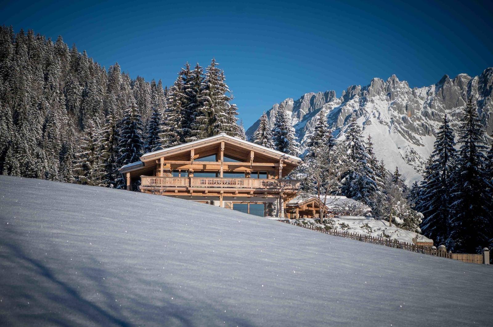 Luxuriöses Holzchalet in verschneiter Berglandschaft mit weitem Blick auf die Alpen.