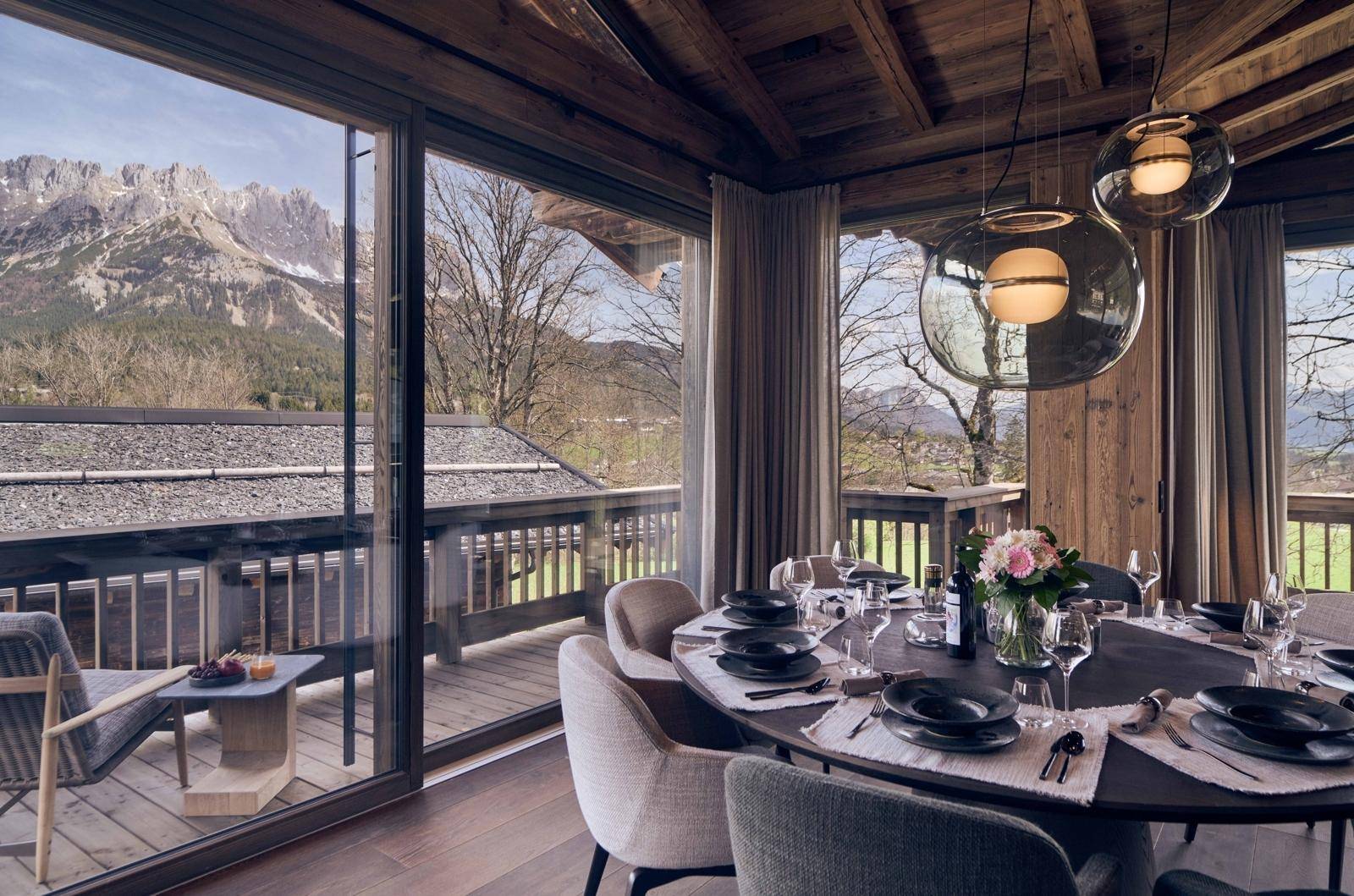 Eleganter Essbereich mit großem Holztisch, modernen Pendelleuchten und beeindruckendem Bergblick.