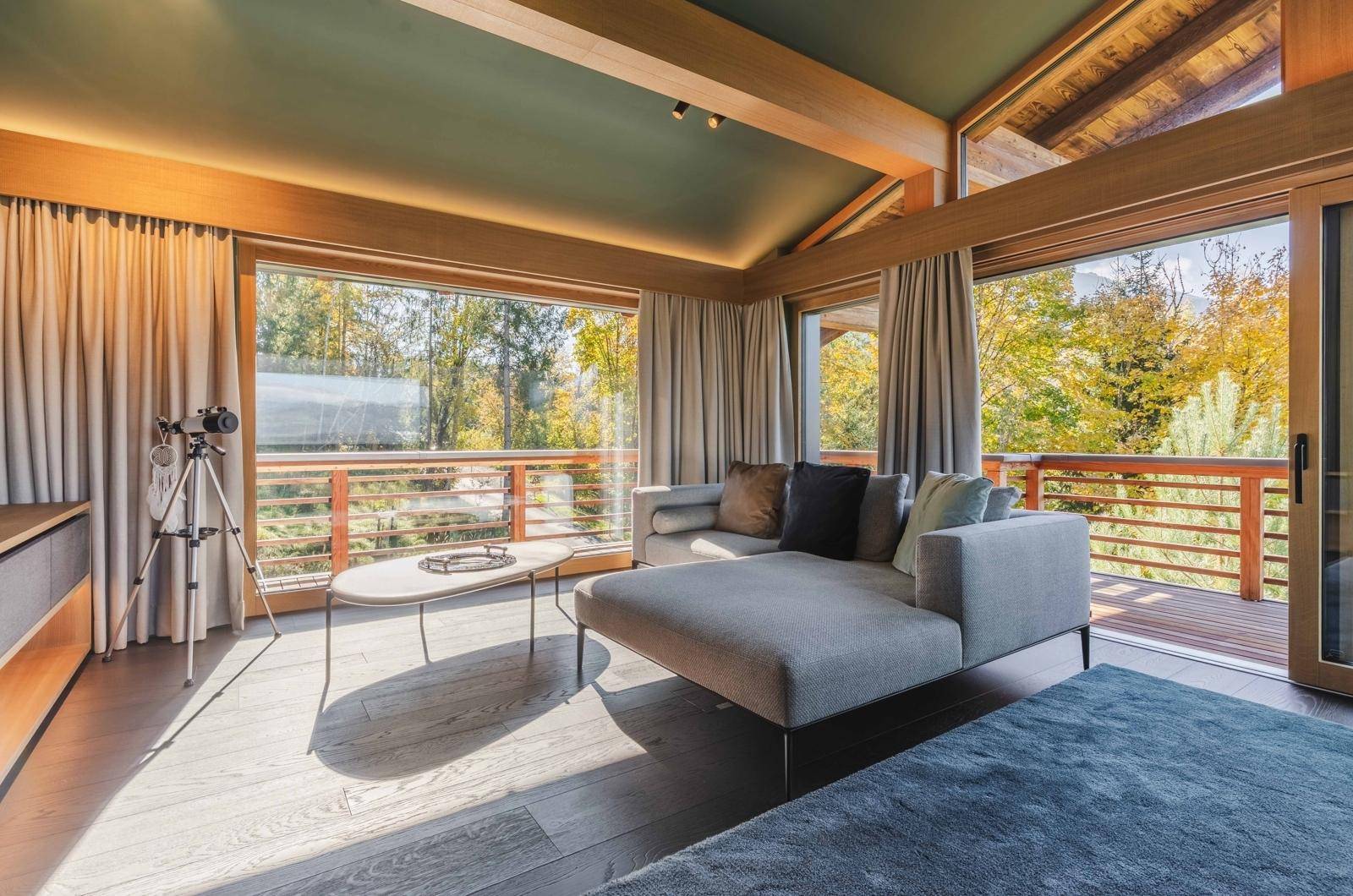 Helles Wohnzimmer mit bequemer Chaiselongue, großen Fenstern und Blick auf die umliegende Natur.