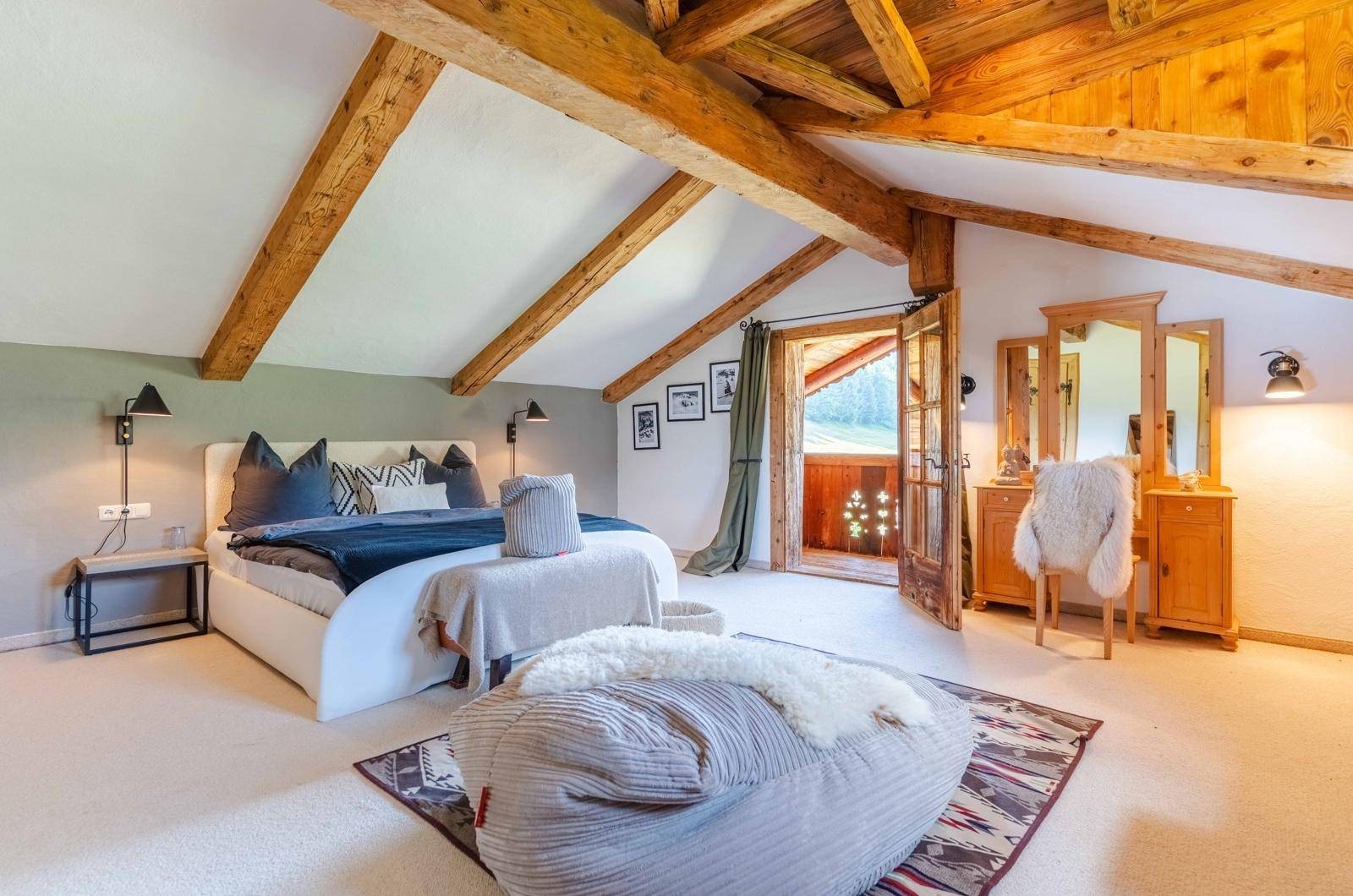 Geräumiges Schlafzimmer mit Holzbalken, Dachschräge und Zugang zu einem charmanten französischen Balkon.