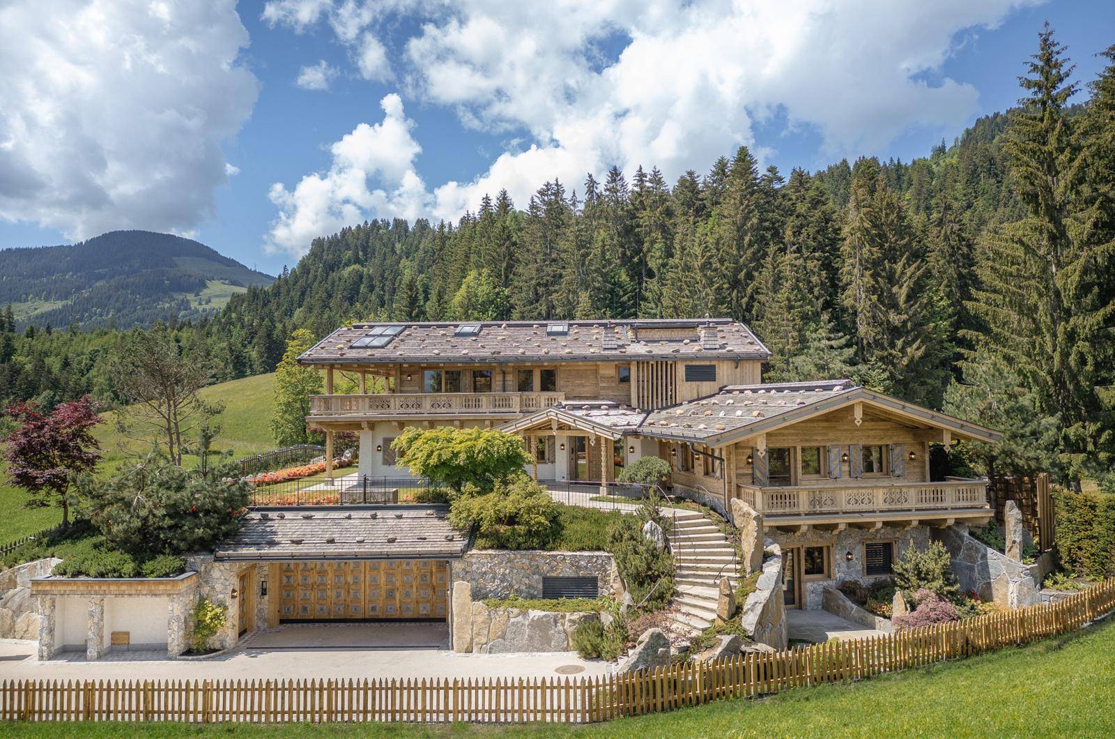 Frontansicht des luxuriösen Holzchalets mit Balkonen, Garage und beeindruckendem Bergpanorama.