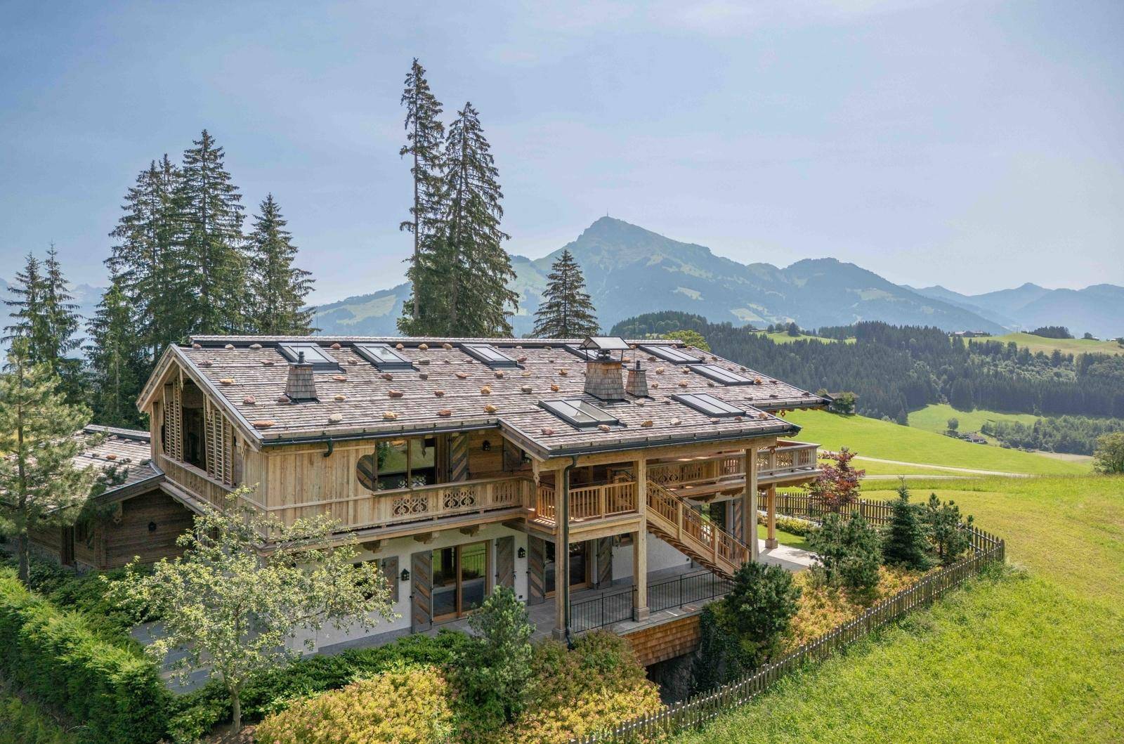 Seitenansicht des luxuriösen Holzchalets mit mehreren Balkonen und weitem Blick auf die Alpenlandschaft.