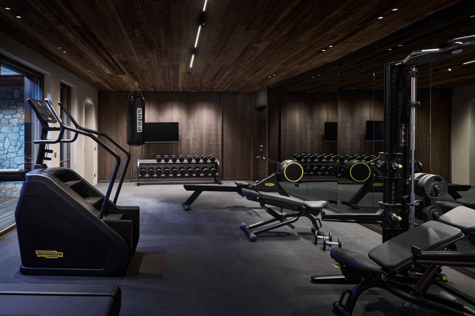 Gut ausgestatteter Fitnessraum mit verschiedenen Trainingsgeräten und dunkler Holzverkleidung.