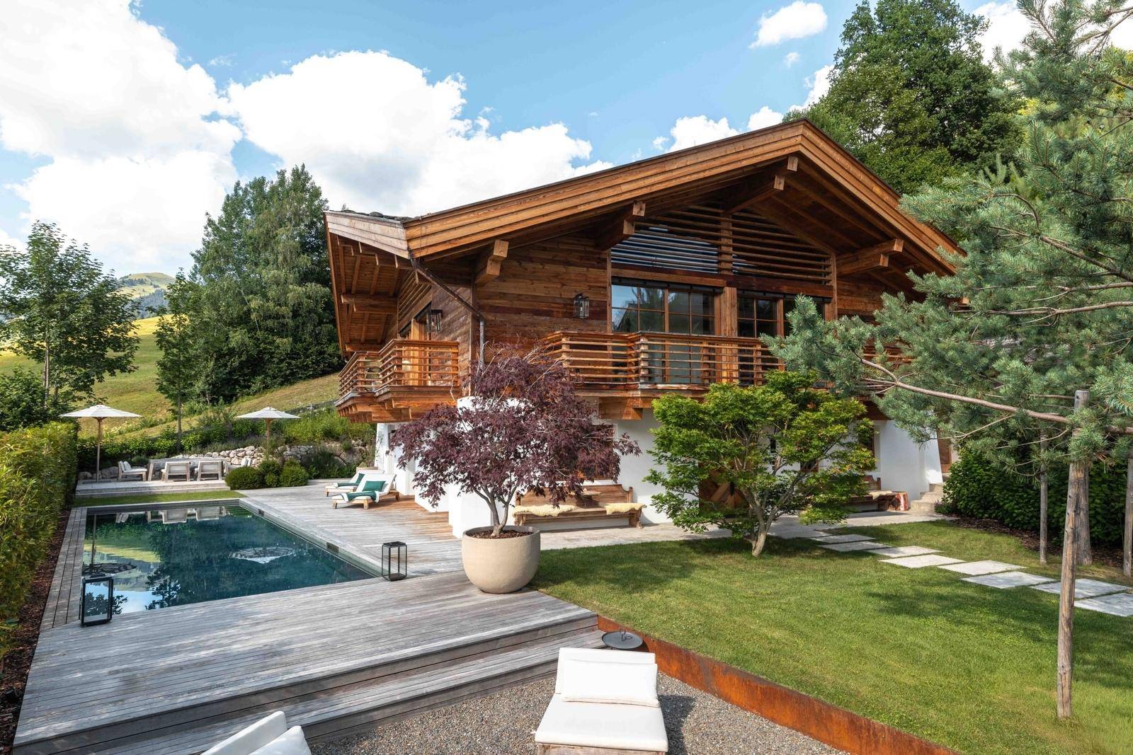 Charmantes Holzchalet mit Balkonen, Pool und gepflegtem Garten vor alpiner Kulisse.