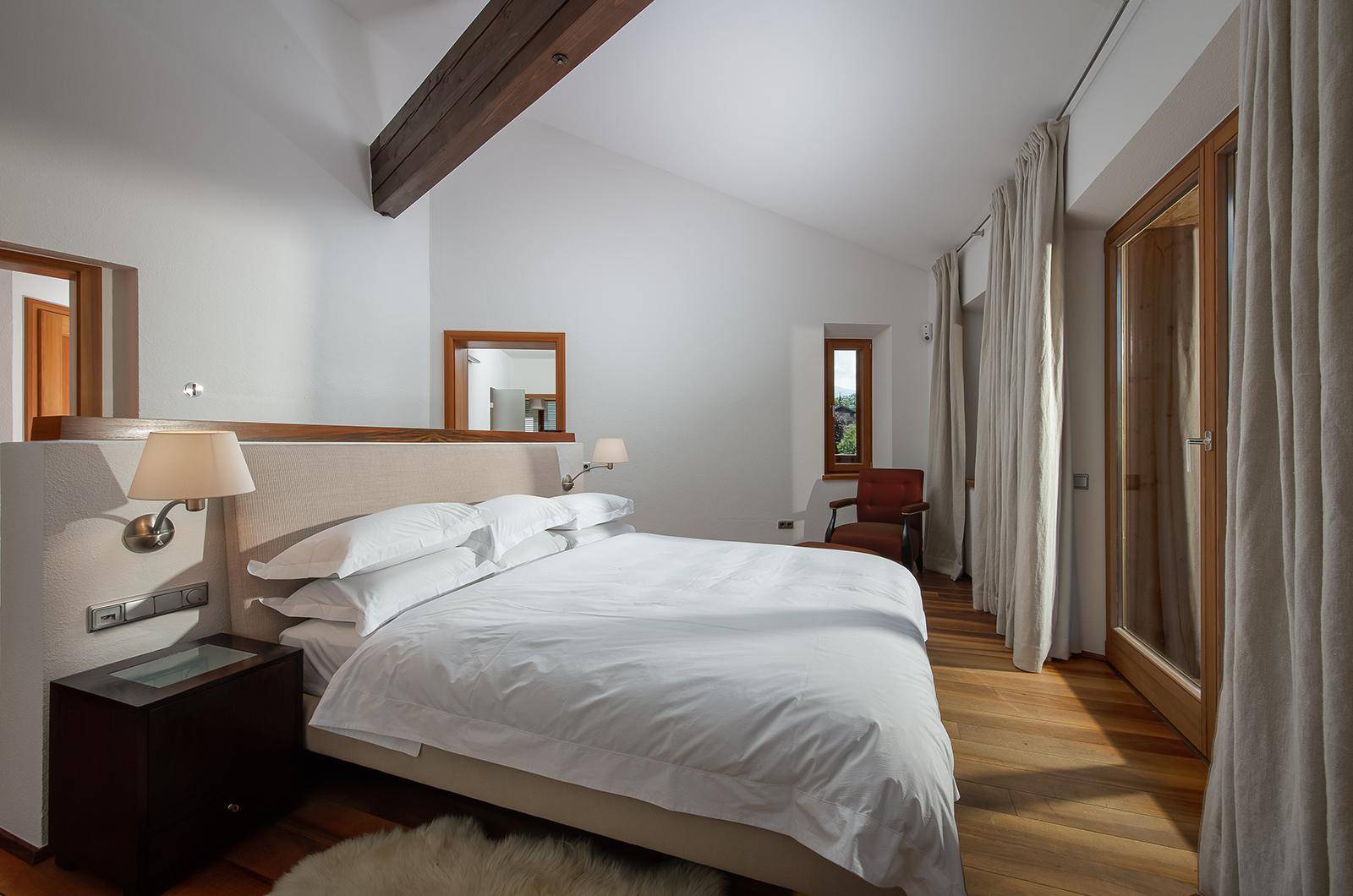 Schlafzimmer mit Holzboden, freiliegendem Holzbalken und Zugang zu einem Außenbereich.