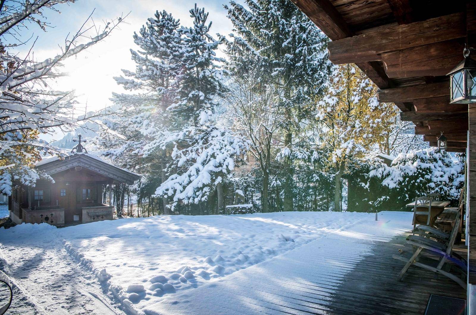 Verschneite Terrasse mit Holzboden und Blick auf den winterlichen Garten und ein kleines Nebengebäude.