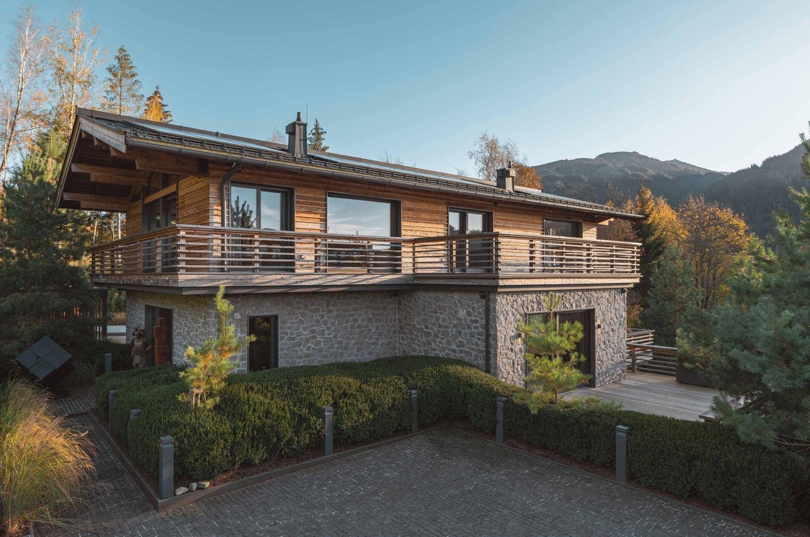 Elegantes Chalet mit einer Kombination aus Stein- und Holzfassade, umgeben von gepflegten Hecken und Bergpanorama.