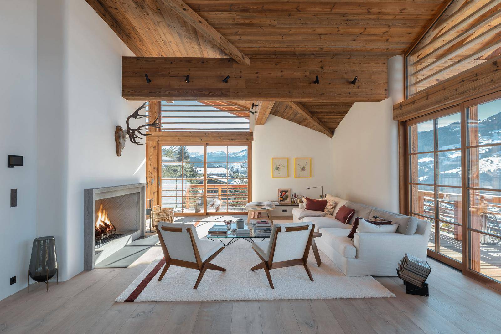 Geräumiges Wohnzimmer mit Kamin, Holzbalkendecke und großen Fenstern mit Bergblick.