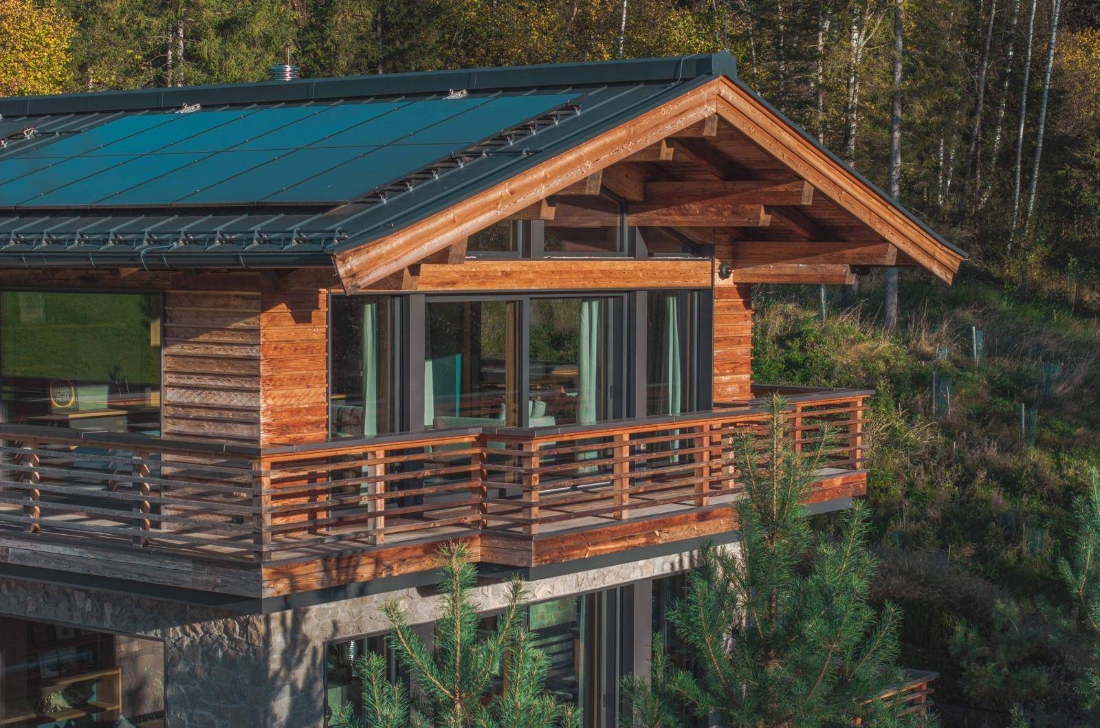 Detailansicht der Holzfassade mit großen Fenstern und einem Balkon, der sich in die alpine Landschaft einfügt.