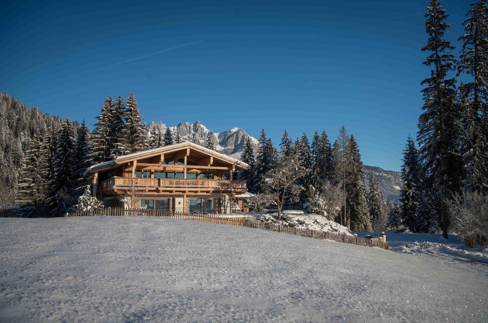 Luxuriöses Holzchalet in verschneiter Umgebung mit Blick auf die umliegenden Berge.