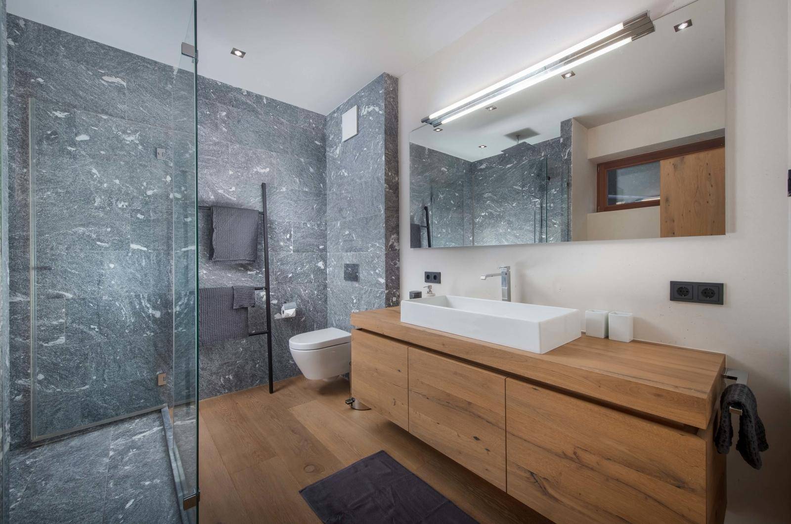 Modernes Badezimmer mit begehbarer Dusche, Holzwaschtisch und eleganten grauen Steinfliesen.