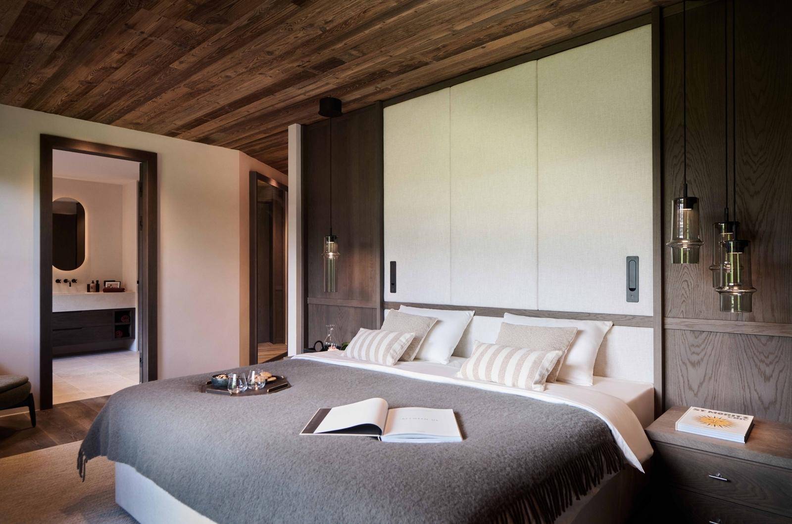 Gemütliches Schlafzimmer mit Holzbalkendecke, großem Bett und Zugang zu einem modernen Badezimmer.